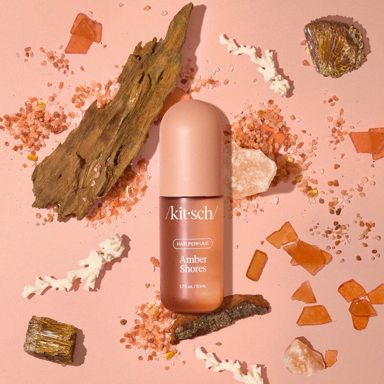 Amber Shores Hair Perfume bottle with pink cap on pink backdrop, surrounded by amber, driftwood, and sea salt crystals.