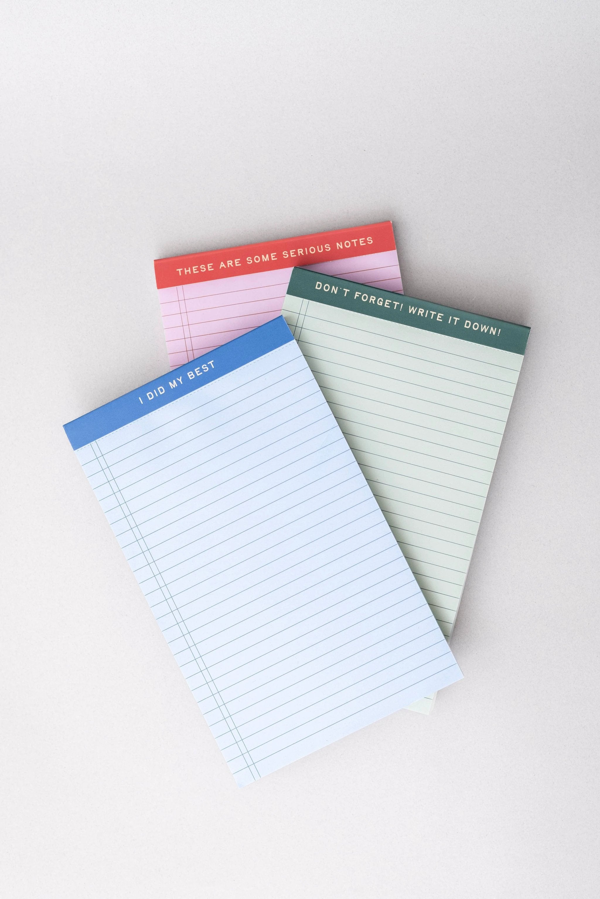 Three mini legal pads in blue, pink, and green, each featuring a unique header phrase.