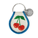 Keychain with embroidered cherries and 'Three Potato Four' tag on a white background
